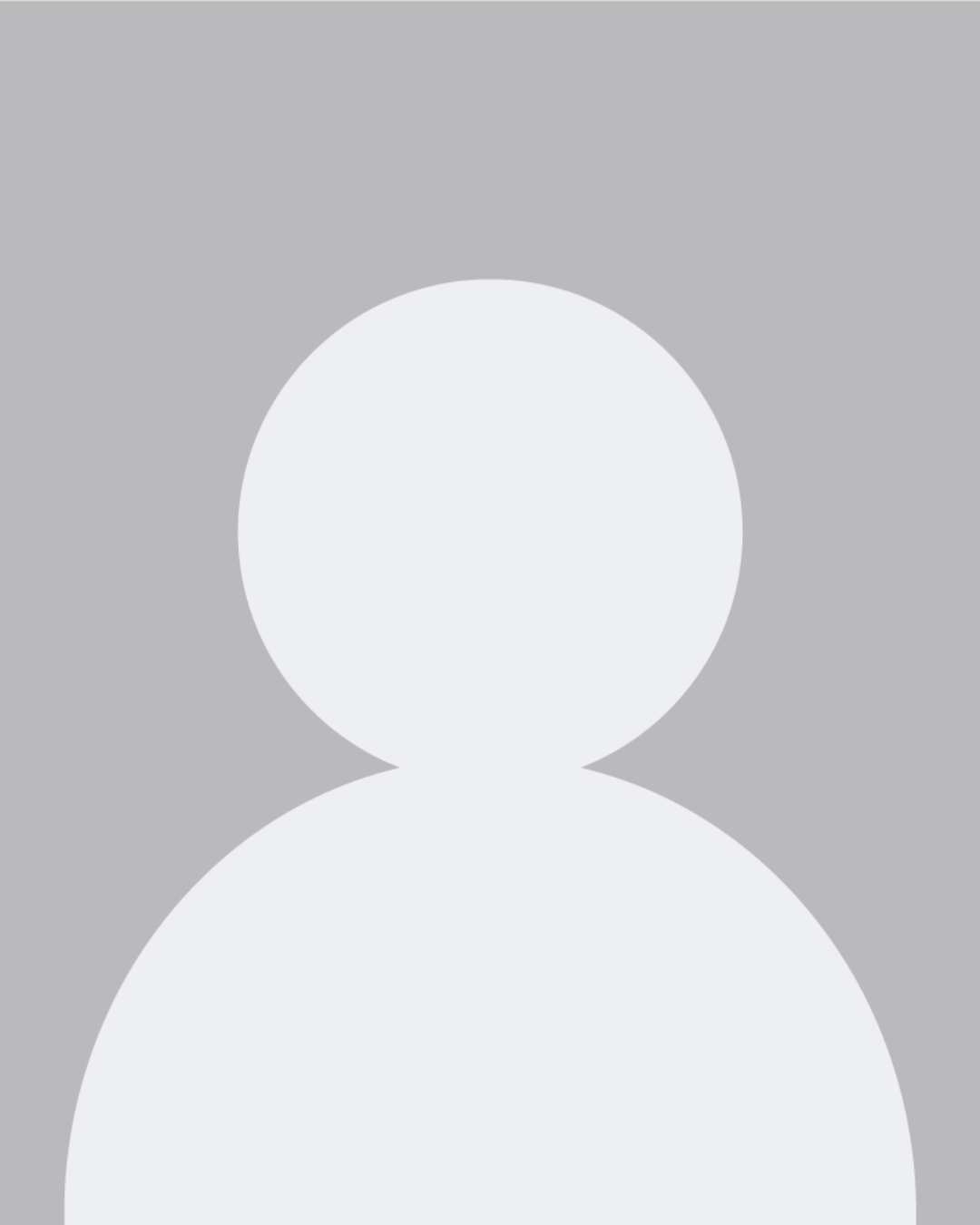 Stephanie, a white woman in a flowery shirt and grey dress pants, smiles at the camera while sitting in a wheelchair.